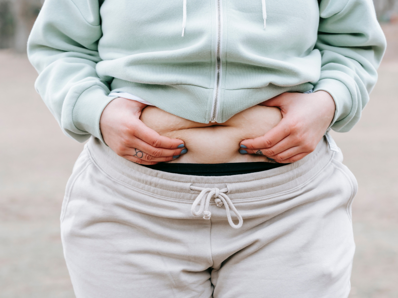 Frustrated woman examining stubborn belly fat in the mirror